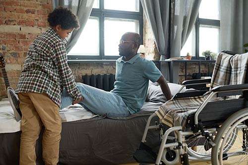 Son helping his disabled father from a bed to a wheelchair