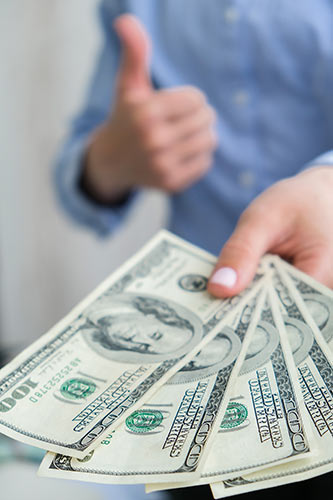 Woman holding out a fan of hundred dollar bills, giving a thumbs-up gesture