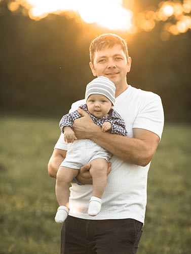 Young dad holding his adorable baby in a park, with the setting sun behind them